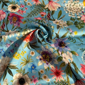 Puede incluir: Una tela vibrante con un estampado floral sobre un fondo azul claro. El diseño incluye varias flores en tonos rosa, rojo, morado, blanco y amarillo, junto con follaje verde. Adecuado para ropa o decoración del hogar.