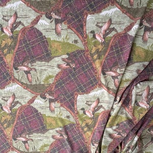 May include: Fabric with a repeating pattern of flying ducks, plaid-like shapes, and a landscape background in shades of green, brown, and burgundy. The fabric has a vintage or rustic aesthetic.