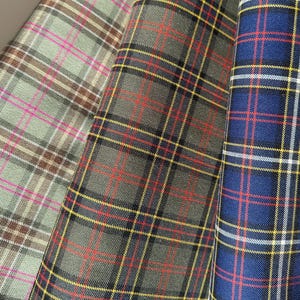 May include: Three different plaid fabrics. One is a green and brown plaid with pink stripes, one is a green and black plaid with red and yellow stripes, and one is a blue plaid with red, yellow, and white stripes.