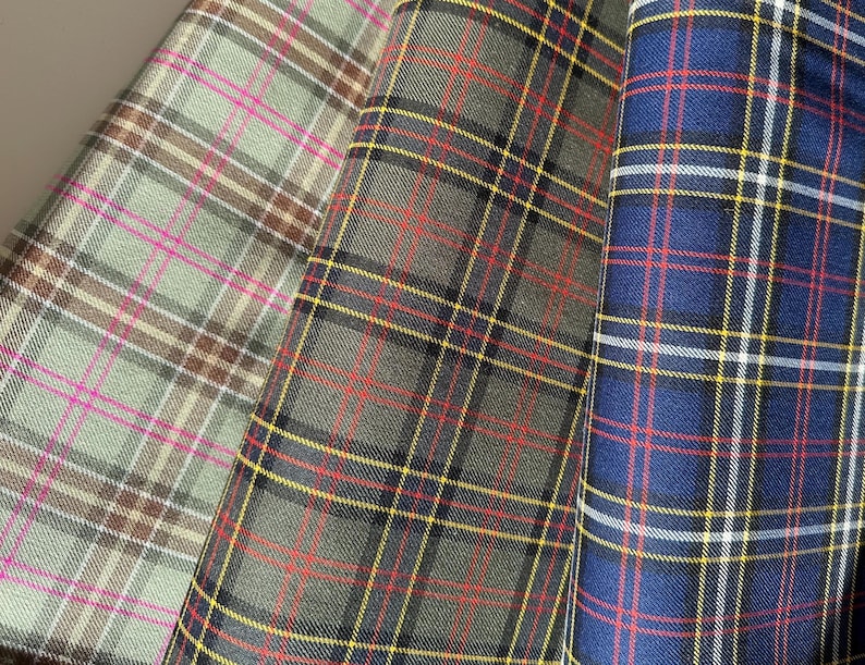 May include: Three different plaid fabrics. One is a green and brown plaid with pink stripes, one is a green and black plaid with red and yellow stripes, and one is a blue plaid with red, yellow, and white stripes.