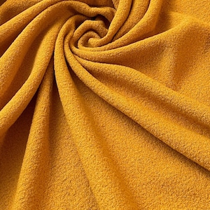 May include: A close-up of a soft, yellow fabric with a textured surface. The fabric is folded and draped in a spiral pattern.