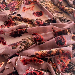 May include: A close-up of a pink sheer fabric with a velvet floral pattern. The flowers are in shades of red, orange, and brown.