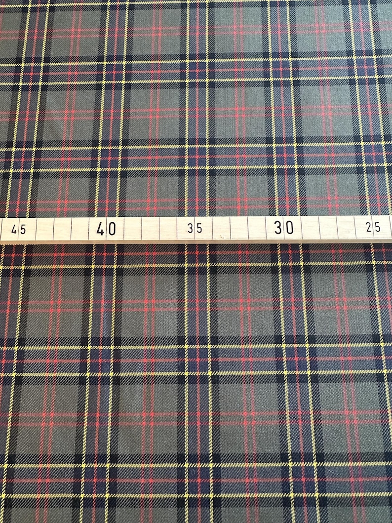 May include: A close-up of a gray, red, and yellow plaid fabric. A ruler is visible at the bottom of the image with markings for 45, 40, 35, 30, and 25.