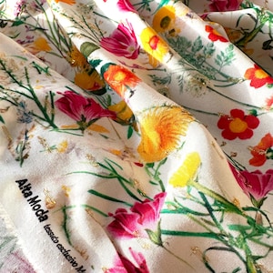 May include: White fabric with a floral print featuring pink, yellow, and red flowers. The fabric has a gold thread woven into the design. The fabric has a label that reads "Alta Moda tessuto esclusivo Made in Italy."