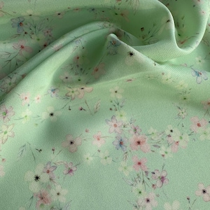 May include: A light green fabric with a delicate floral pattern in shades of pink, blue, and white. The fabric has a soft, flowing texture.