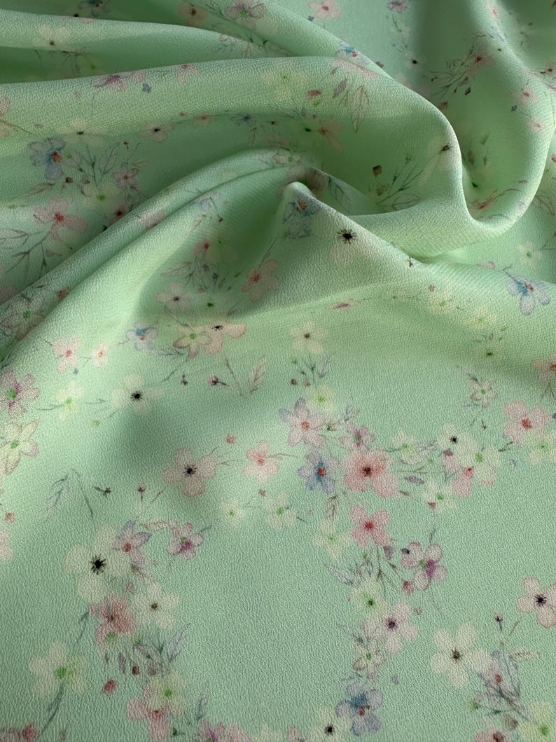 May include: A light green fabric with a delicate floral pattern in shades of pink, blue, and white. The fabric has a soft, flowing texture.