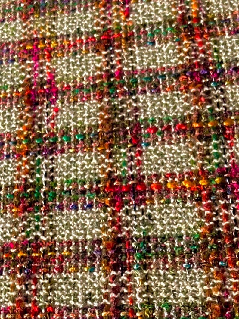 Puede incluir: Primer plano de una tela tejida con un patr&oacute;n de cuadros. La tela es de color beige claro con hilos de rojo, naranja, verde, azul y morado.