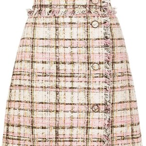 Puede incluir: Una falda de cuadros rosa y blanca con un dobladillo deshilachado y botones marrones. La falda est&aacute; hecha de tejido de tweed.