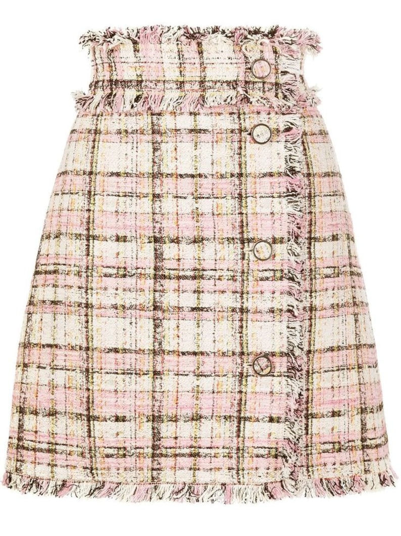 Puede incluir: Una falda de cuadros rosa y blanca con un dobladillo deshilachado y botones marrones. La falda est&aacute; hecha de tejido de tweed.