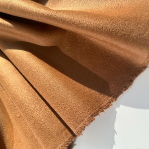 May include: Close-up of a folded piece of brown fabric with a soft, textured surface. The fabric has a raw, unfinished edge and is draped to show the texture and color variations.