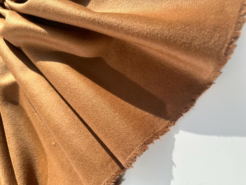 May include: Close-up of a folded piece of brown fabric with a soft, textured surface. The fabric has a raw, unfinished edge and is draped to show the texture and color variations.