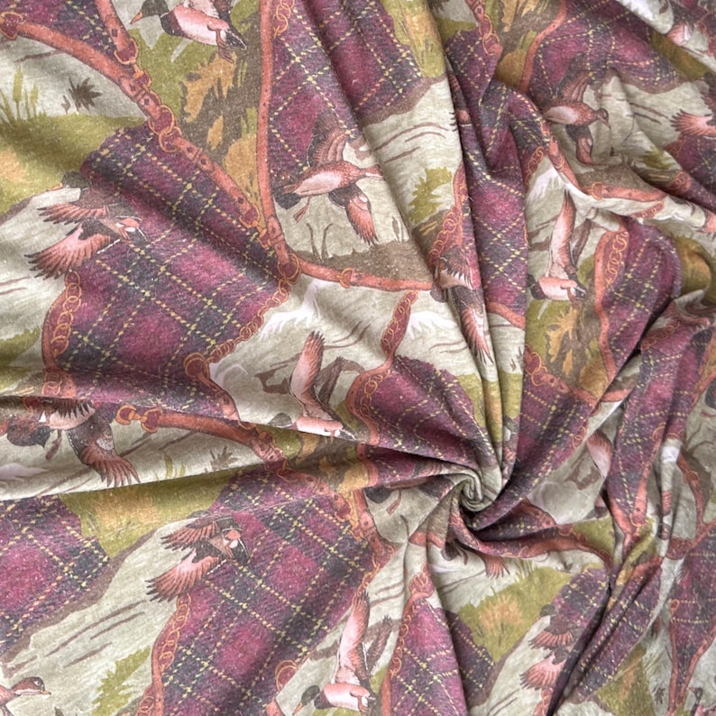 May include: Fabric with a repeating pattern of flying ducks, plaid squares, and decorative chain-like borders. The color palette includes shades of burgundy, brown, green, and beige. The fabric is likely used for apparel or home decor.