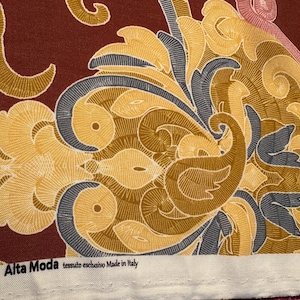 May include: A close-up of a fabric with a paisley pattern in shades of brown, yellow, blue, and pink. The fabric has a white border with the text "Alta Moda tessuto esclusivo Made in Italy".