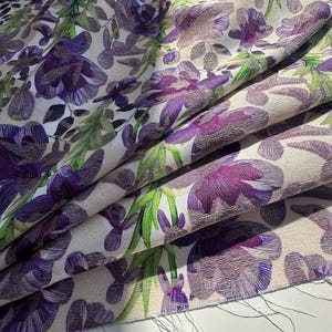 May include: Purple floral fabric with a white background. The fabric has a textured surface and a subtle sheen.