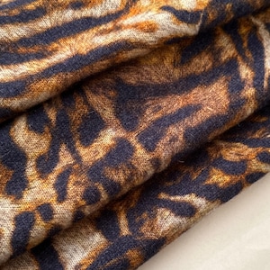 May include: Close-up of a fabric with a tiger stripe pattern. The fabric features a mix of brown, tan, and dark navy blue colours. The material is folded, showing the texture and design of the textile. The overall look is reminiscent of animal print.