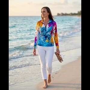 May include: A long-sleeved quarter-zip pullover featuring a vibrant, multi-coloured paint splatter pattern and a central graphic of a blue winged horse, paired with slim-fit white trousers and a pair of brown flip-flops held in one hand.