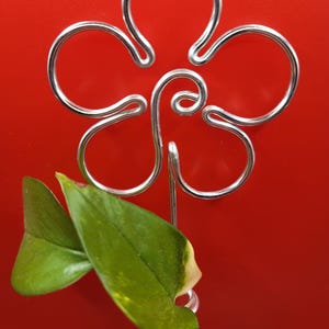 Puede incluir: Un porta plantas de metal plateado con forma de flor con una sola hoja verde y amarilla en un tubo de vidrio transparente.