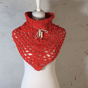Op de afbeelding: Een felrode gehaakte colwarmer. De handgemaakte nekwarmer heeft een hoge kraag en een decoratieve stropdas met houten kralen. Het open weefselontwerp voegt een unieke textuur toe aan dit gezellige accessoire.
