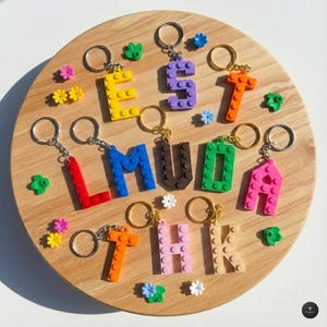 Pode incluir: Uma coleção de chaveiros de letras construídos com blocos de montar de plástico coloridos. As letras E, S, T, L, M, U, D, A, T, H e K são exibidas em várias cores, incluindo amarelo, roxo, laranja, vermelho, azul, marrom, verde, rosa e bege.