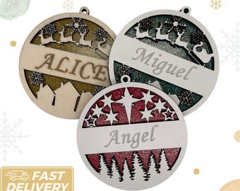 May include: Three round wooden Christmas ornaments with glitter and a white background. The ornaments are decorated with a winter scene and have the names "Alice", "Miguel", and "Angel" written on them.