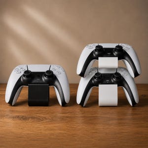 以下が含まれることがあります： 白と黒のワイヤレスゲームコントローラー3台。1台は黒いスタンドに置かれ、他の2台は白いスタンドに垂直に積み重ねられています。各コントローラーには、2つのアナログスティック、方向パッド、アクションボタンが備わっています。