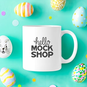 May include: White ceramic mug with a black inscription that reads "hello mock shop" surrounded by colorful Easter eggs on a turquoise background.