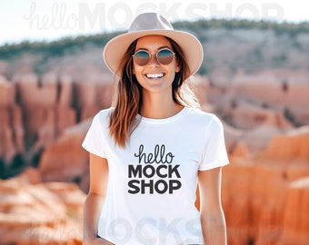 May include: A white t-shirt with the text "hello mock shop" printed on the front. The shirt is being worn by a person wearing a straw hat and sunglasses. The person is standing in front of a rocky, desert-like landscape.