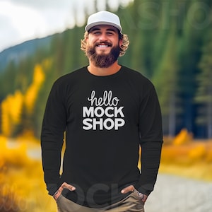 May include: A man wearing a black long-sleeve shirt with the text "hello MOCK SHOP" in white. He is wearing a white baseball cap and has a beard.