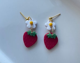 May include: A pair of red strawberry earrings with white daisy flowers and green leaves. The earrings have gold hooks.