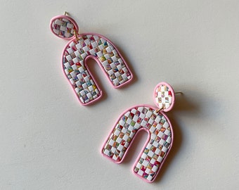 May include: A pair of pink and white checkerboard arch earrings. The earrings are made of polymer clay and have a pink outline.