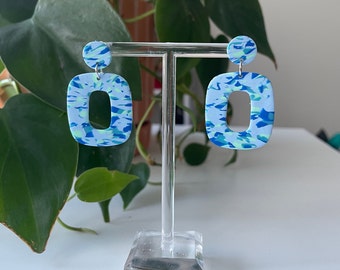 May include: A pair of blue and green patterned rectangle shaped earrings with a silver hook.