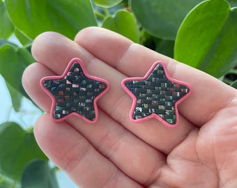 May include: A pair of pink star-shaped earrings with a black and white patterned center.