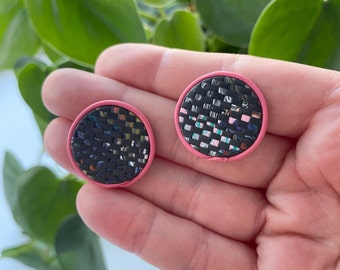 May include: Two round earrings with a black and white woven pattern and a pink border.