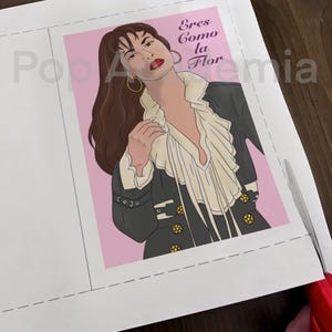 May include: A pink background with a drawing of a woman with long brown hair wearing a black jacket with gold buttons and a white blouse. The text "Eres Como La Flor" is written in purple above the woman's head.