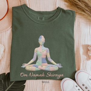 May include: Moss green t-shirt featuring a patchwork design of a person in a yoga pose. The text "Om Namah Shivaya" is below the image, with "Moss" printed below that. White sneakers are visible in the bottom right corner.