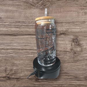 May include: A clear glass tumbler with a bamboo lid and straw. The tumbler features a black graphic design with the word "Goosebumps" and other text. The tumbler is on a black rotating stand.