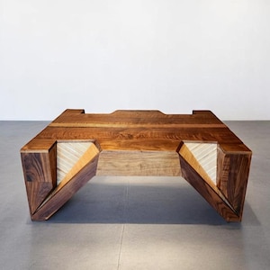 Puede incluir: Una mesa de centro contemporánea de madera oscura, con un diseño geométrico. La parte superior rectangular tiene una sección empotrada, y las patas anguladas revelan un interior claro y rayado. El diseño de la mesa combina madera natural con estética moderna.