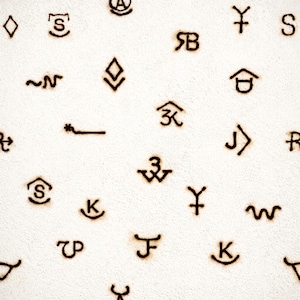May include: Close-up of a white textured surface with various brown-colored ranch brands. The brands are scattered across the surface, featuring different shapes and symbols, including letters and geometric designs.