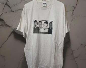 May include: A white short-sleeved t-shirt featuring a black and white image of four people. The image is rectangular and centered on the shirt. The shirt is hanging on a white hanger.