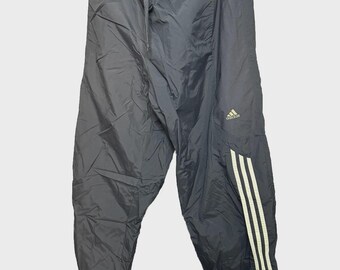 May include: Black Adidas track pants with three white stripes down the side. The pants have a drawstring waist and the Adidas logo is visible on the upper leg. The material appears to be a lightweight nylon.