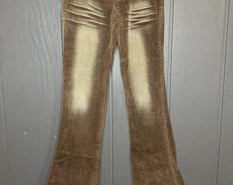 May include: Brown corduroy pants with a faded, light-colored design down the front. The pants have a flared leg opening and a raw hem. The pants are hanging on a white hanger.