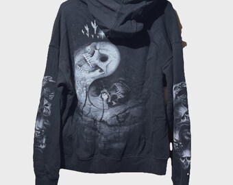 May include: Black hooded sweatshirt with a large Yin Yang skull design on the back. The sleeves feature skull graphics. The design is in shades of gray and white, creating a striking contrast against the black fabric.