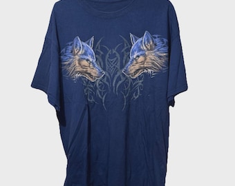 May include: Navy blue t-shirt featuring two wolf heads facing each other, with blue and brown fur details. A tribal design is between the wolf heads. The shirt is hanging on a white hanger.