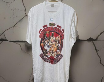 May include: White t-shirt featuring a graphic of the 1991 NBA Champion Chicago Bulls team. The design includes the words "1991 NBA Champs" and the team's name. The shirt is hanging on a white hanger.