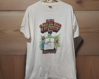 May include: Off-white t-shirt with a colorful graphic. The graphic features the text "3rd Annual Shot Six Holes In My Freezer Party" above an illustration of people and a freezer. The date "February 17th, 1996" and location "Madison Wisconsin" are also included.