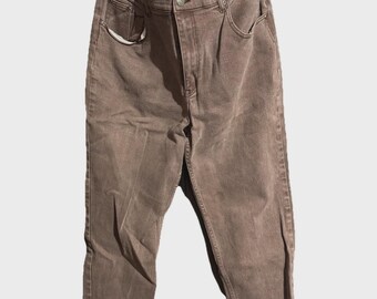 May include: Brown denim jeans with a button closure, front pockets, and a classic five-pocket design. The jeans are hanging on a metal hanger against a white background. The jeans have a faded appearance.