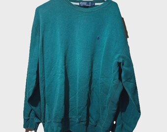 May include: Teal green crew neck sweatshirt with a small navy blue logo on the chest. The long-sleeved top is hanging on a white hanger. The sweatshirt has a ribbed hem and cuffs.