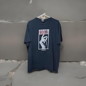 May include: Dark navy blue t-shirt with a graphic design featuring a hand gesture and the word "memphis" in white. The graphic is in a rectangular frame with red accents. The shirt is hanging on a white hanger.