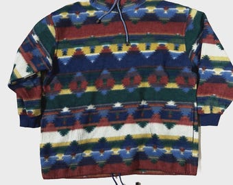 May include: A multi-colored fleece pullover with a geometric pattern. The colors include red, blue, green, yellow, and white. It has a high collar with a drawstring and a front pocket. The cuffs and bottom hem are a solid navy blue.