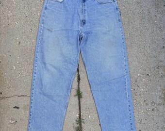 May include: Light blue denim jeans with a classic five-pocket design. The jeans have a straight leg cut and a faded wash, giving them a vintage look. The jeans are laid flat on a concrete surface.